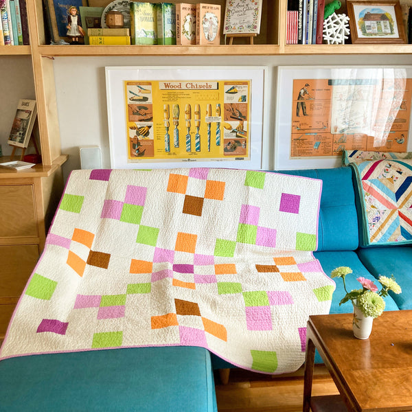 Dolly Mix quilt on a blue couch with bookshelves behind it